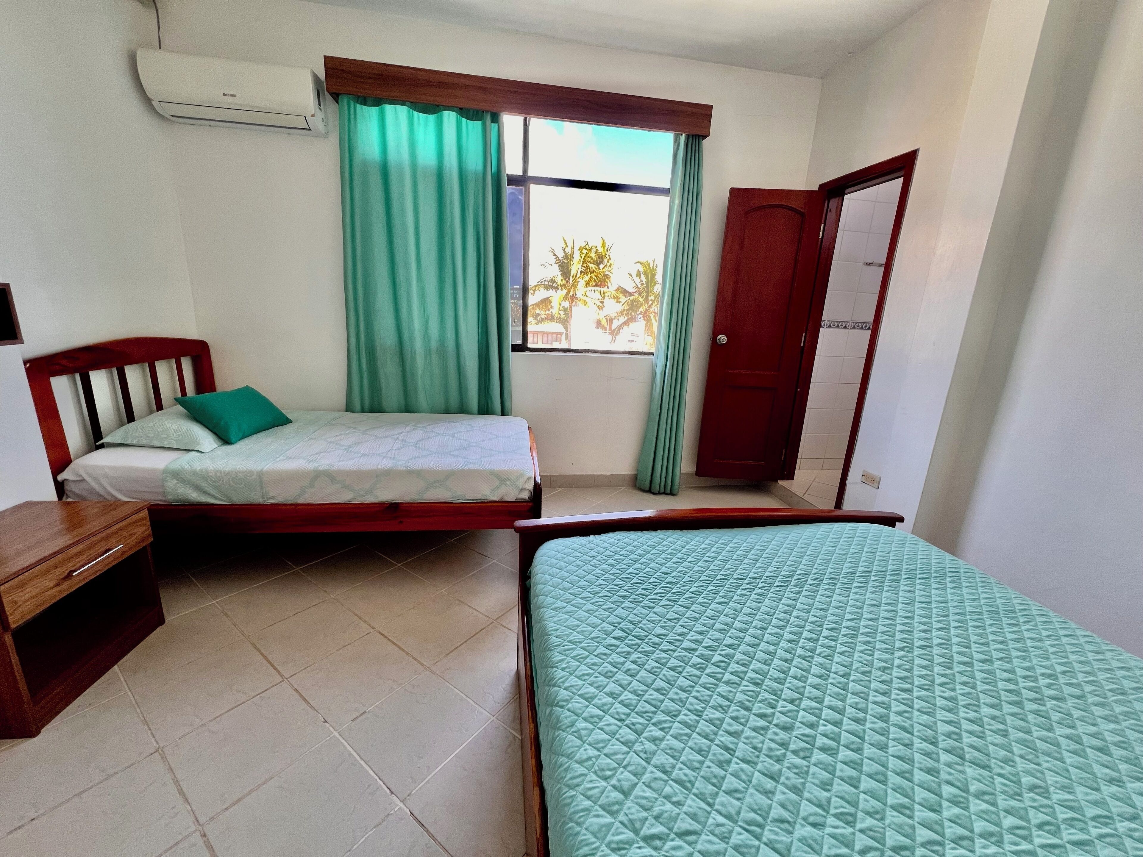 Una habitación con dos camas, un escritorio de madera, una ventana con cortinas y una puerta.