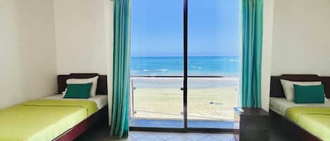 A room with two beds, a view of the beach, and a wooden ceiling.