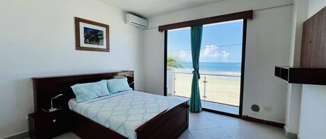 Un dormitorio con cama, un cuadro en la pared, un equipo de aire acondicionado y vista a la playa a través de una puerta corrediza.