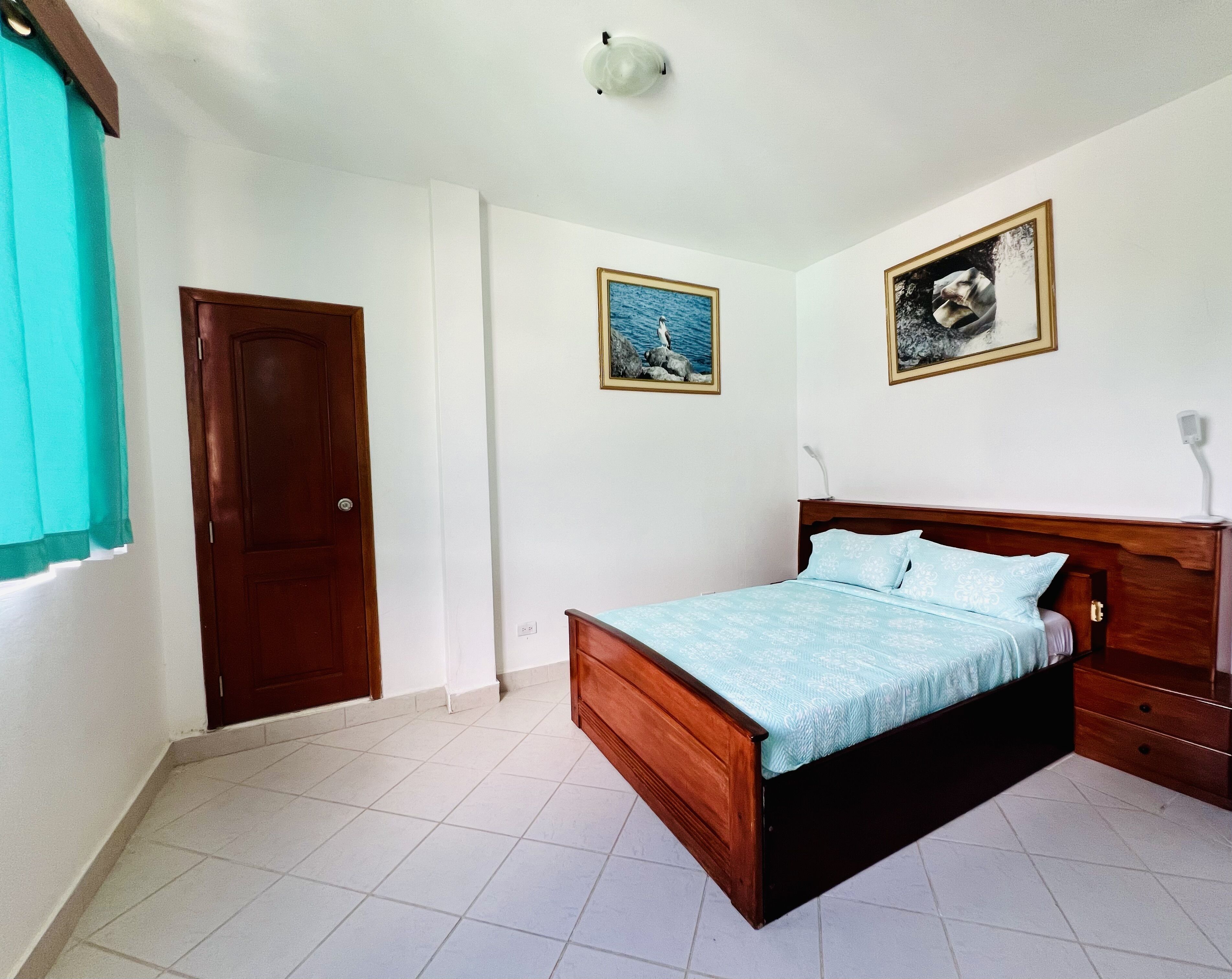 A bedroom with a wooden bed, white walls, and two framed pictures.