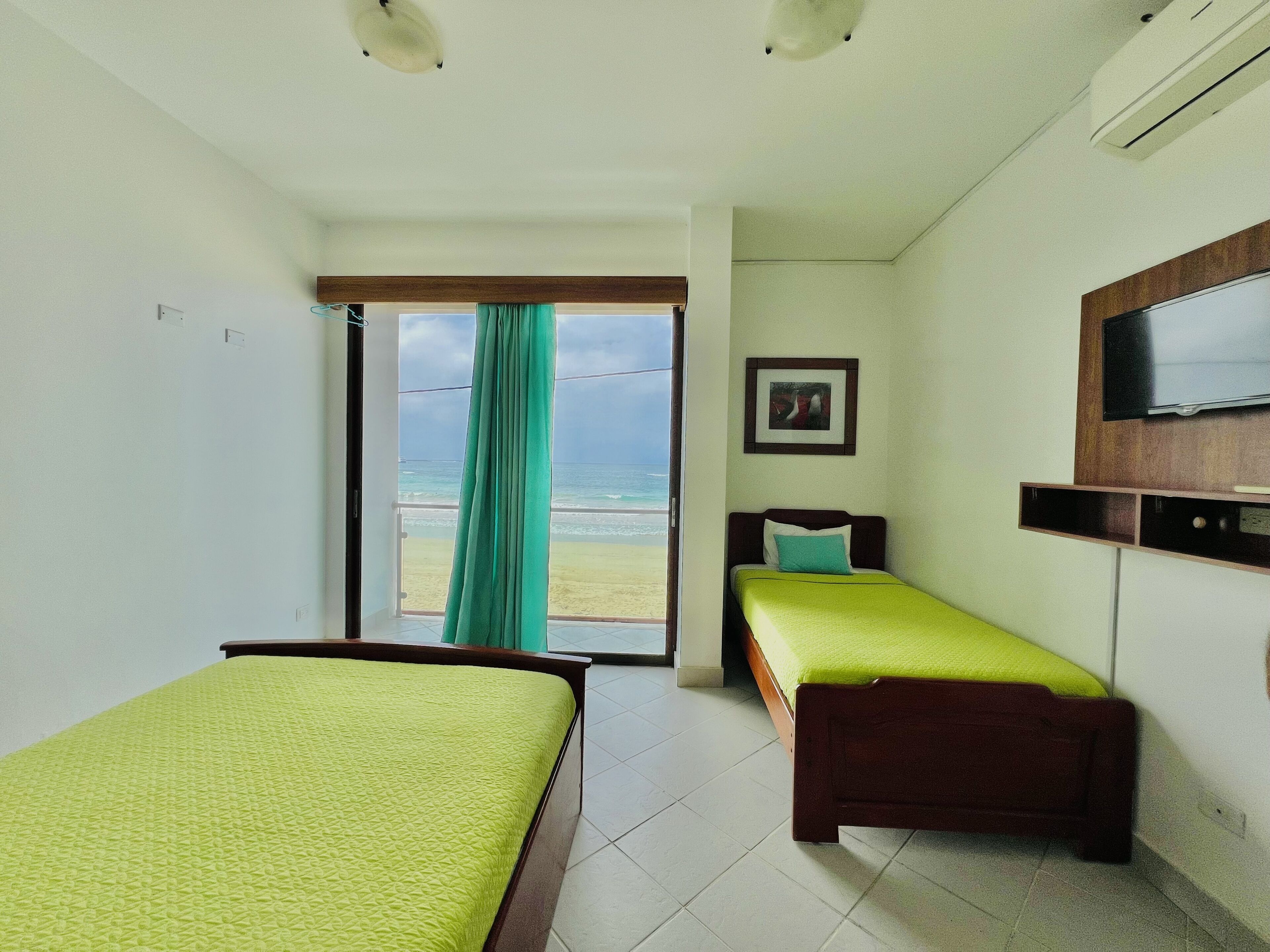 Habitación de hotel con dos camas, un televisor y vista a la playa.