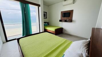 A hotel room with a bed, a TV mounted on the wall, and a view of the beach through the window.
