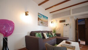 A living room with a sofa, a coffee table, and a chair. There is a painting on the wall, a plant, and a door leading to another room. - 200 Livingtarifa Drago (Tarifa)
