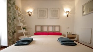 A neatly made bed with red and blue towels, a white bedside table with a small plant, and two wall-mounted light fixtures. - 200 Livingtarifa Drago (Tarifa)