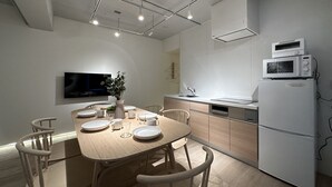 A modern kitchen with a dining table set for four, a microwave, and a built-in oven. - Art BLDG (Hiroshima)
