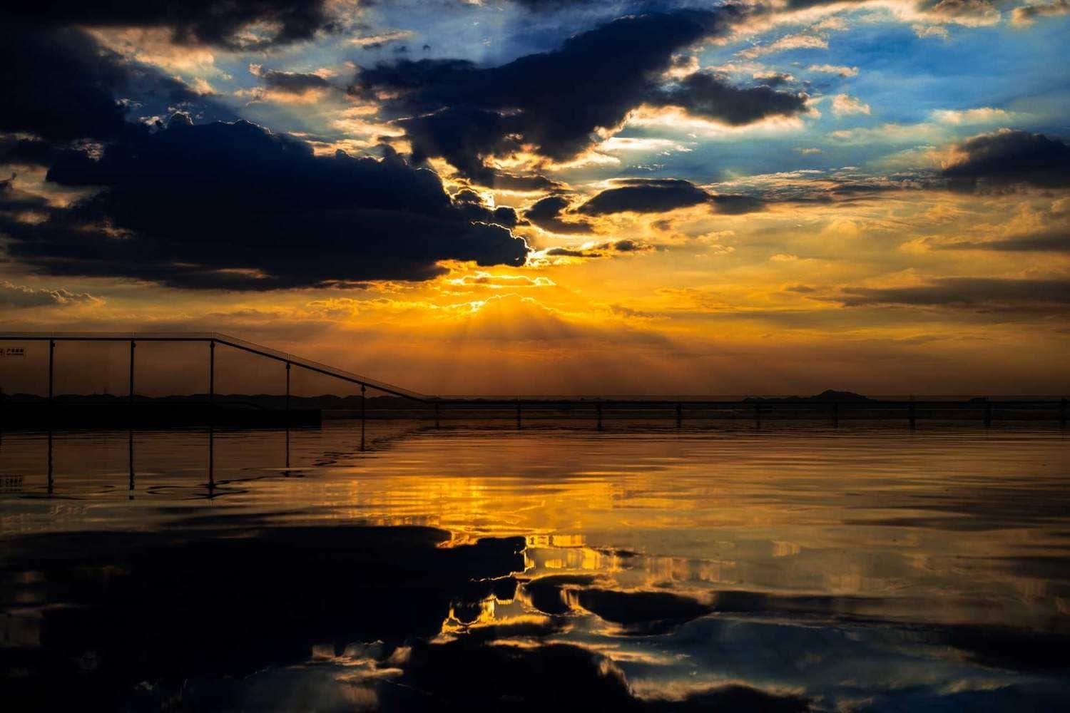 Un atardecer sobre una masa de agua tranquila con una estructura de puente.