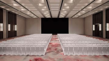 A conference room with rows of white chairs, a patterned carpet, and a dark screen at the front.