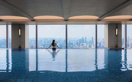 A large indoor swimming pool with a city view, featuring a modern architectural design with large windows and a high ceiling.