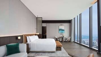 Quarto de hotel moderno com uma cama grande, um sofá, uma escrivaninha e vista para a cidade.