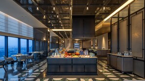 En moderne hotellobby med et centralt morgenmadsområde, siddepladser og store vinduer med udsigt over byen.