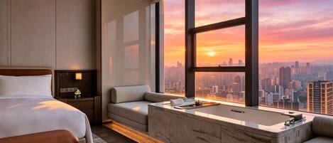 Una habitación de hotel moderna con una cama grande, un sofá, una bañera y vistas a la ciudad al atardecer.