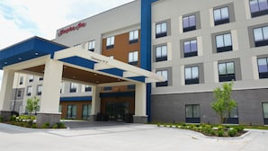 Un hotel Hampton Inn con fachada moderna, un acceso cubierto y un cartel que indica una altura libre de 14 pies.