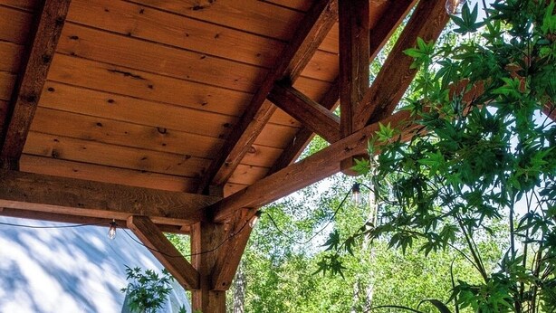 Eine Holzterrasse mit einer großen weißen Badewanne, umgeben von Topfpflanzen und einem Feuerlöscher.