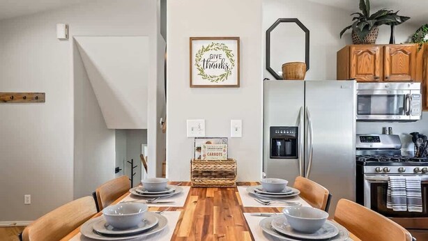 Una cocina moderna con una mesa de comedor de madera para cuatro personas, un refrigerador, un microondas y una estufa.