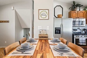 A modern kitchen with a wooden dining table set for four, a refrigerator, a microwave, and a stove.