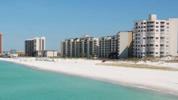 A beachfront hotel with multiple high-rise buildings, a sandy beach, and clear turquoise waters.