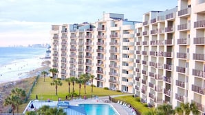 A high-rise hotel with multiple balconies, a pool area, and a beach view.