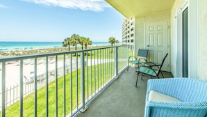 A balcony with a view of the beach, a chair, and a door.