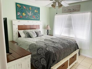Une chambre à coucher avec un lit, un ventilateur de plafond, une décoration murale représentant des poissons et une fenêtre avec des stores.