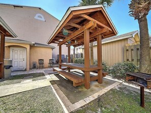 Une structure en bois formant une pergola dans un jardin, avec un espace patio, une porte et une clôture.