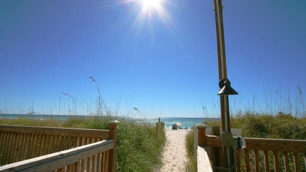 A wooden boardwalk leading to a beach with a clear sky and sun shining. - Mariner West 205 (Panama City Beach)