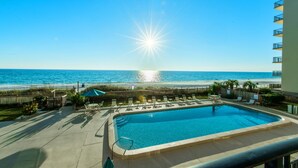 A pool area with a view of the ocean, a sunburst effect, and a wooden fence. - Mariner West 205 (Panama City Beach)
