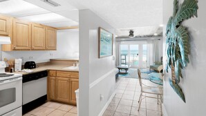 A kitchen with wooden cabinets, a dishwasher, and a stove. There is a dining area with a glass table and chairs. - Mariner West 205 (Panama City Beach)
