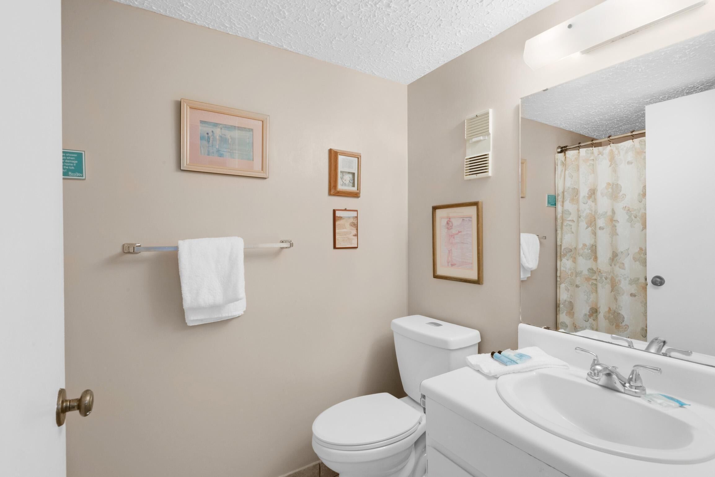A bathroom with a toilet, sink, and mirror. There are framed pictures on the wall and a towel hanging on a rack.