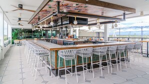 A modern bar area with a long counter, white bar stools, and ceiling fans. - The Perry Hotel Naples (Naples)