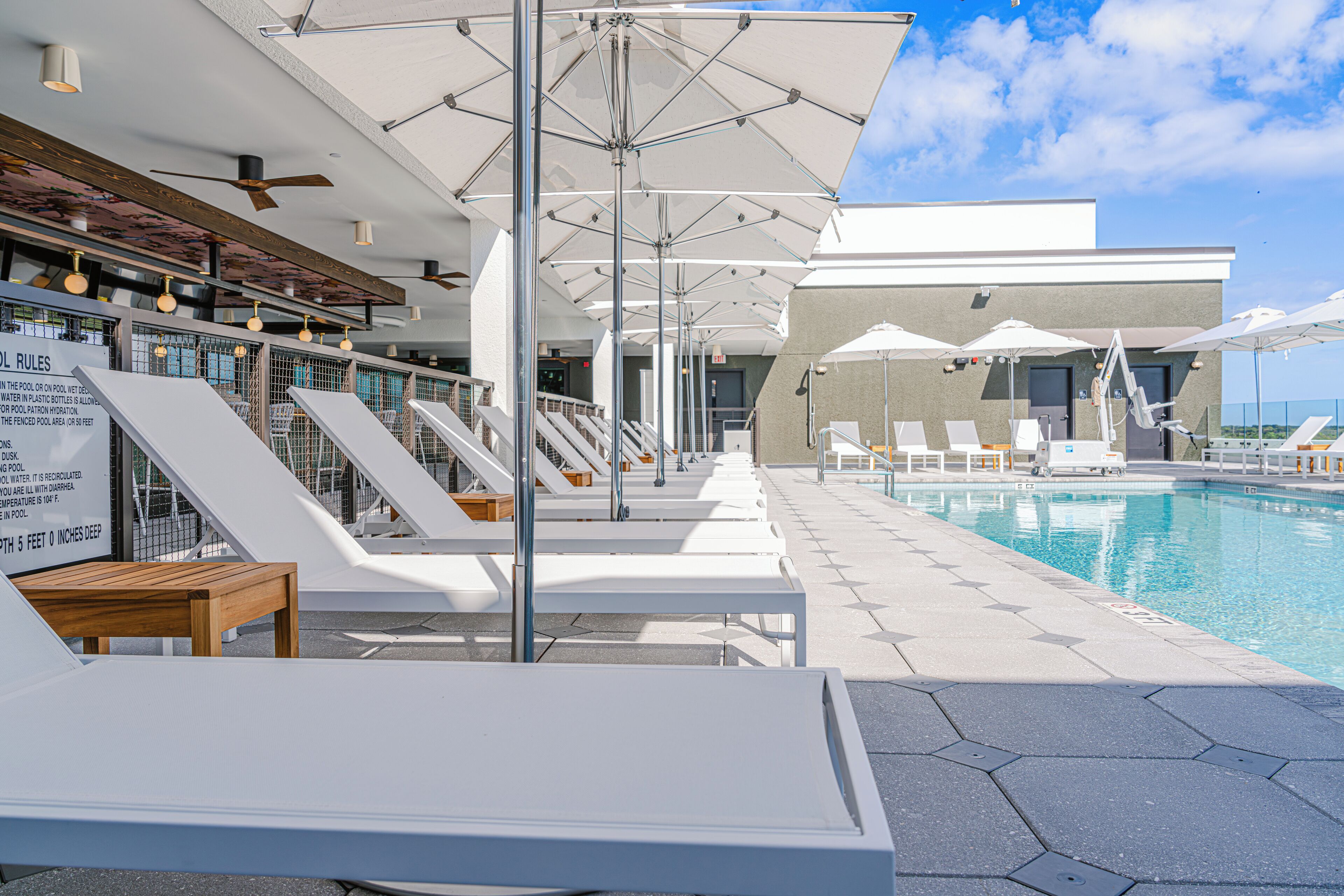 Un espace aménagé au bord de la piscine, avec des chaises longues, des parasols et une piscine.