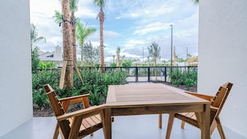 An outdoor patio with a wooden table and chairs, surrounded by palm trees and greenery.