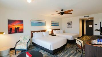 A hotel room with two beds, a desk, a chair, a coffee table, and artwork on the walls.