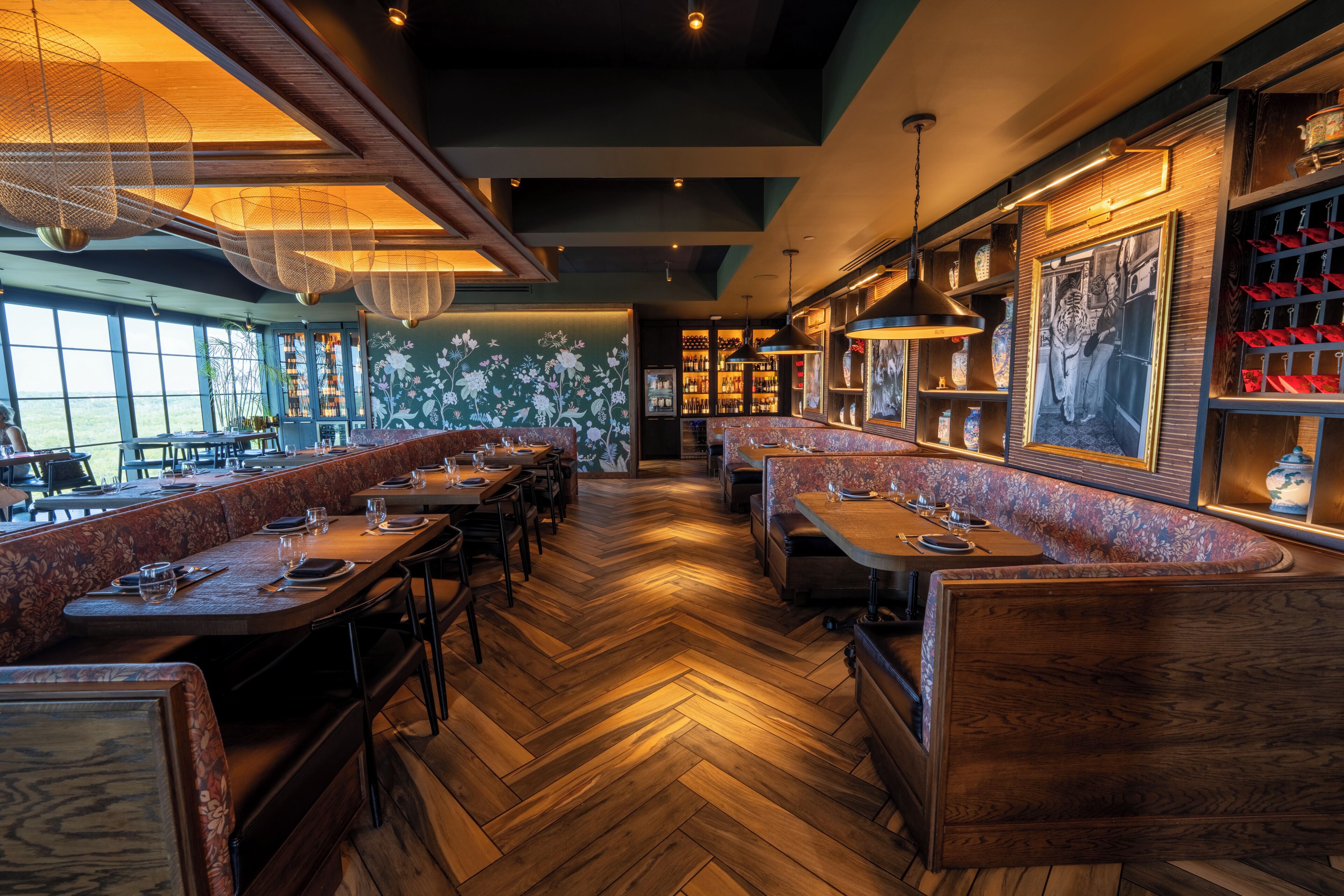A restaurant with wooden flooring, booths, and a bar area with shelves and framed pictures.