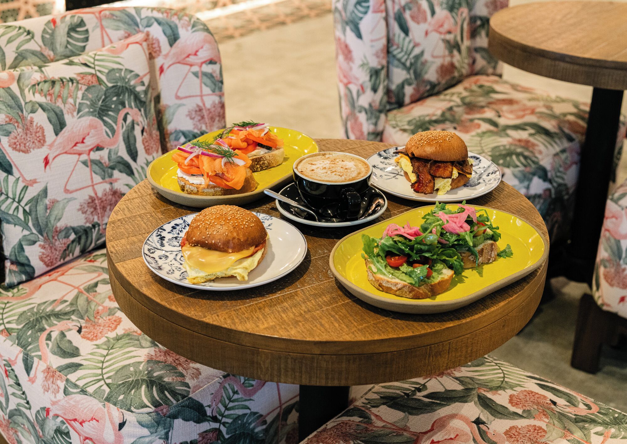 A round wooden table with various food items and a cup of coffee.