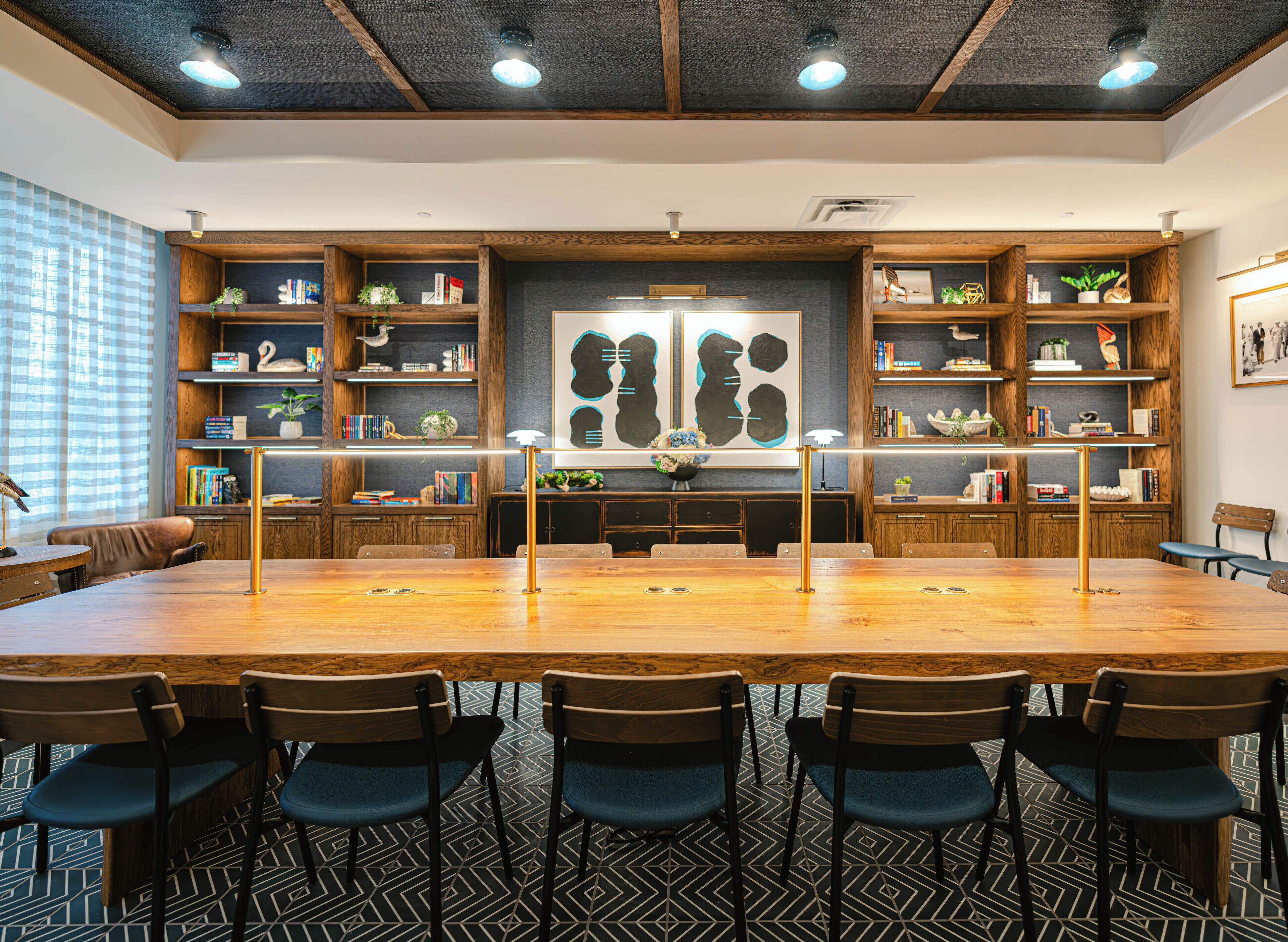 A conference room with a long wooden table, six chairs, and bookshelves filled with books and decorative items.