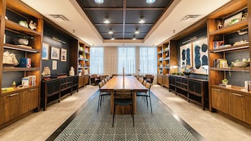 Een ruime eethoek met een lange houten tafel, omringd door stoelen, en grenzend aan houten boekenkasten vol boeken en decoratieve objecten.