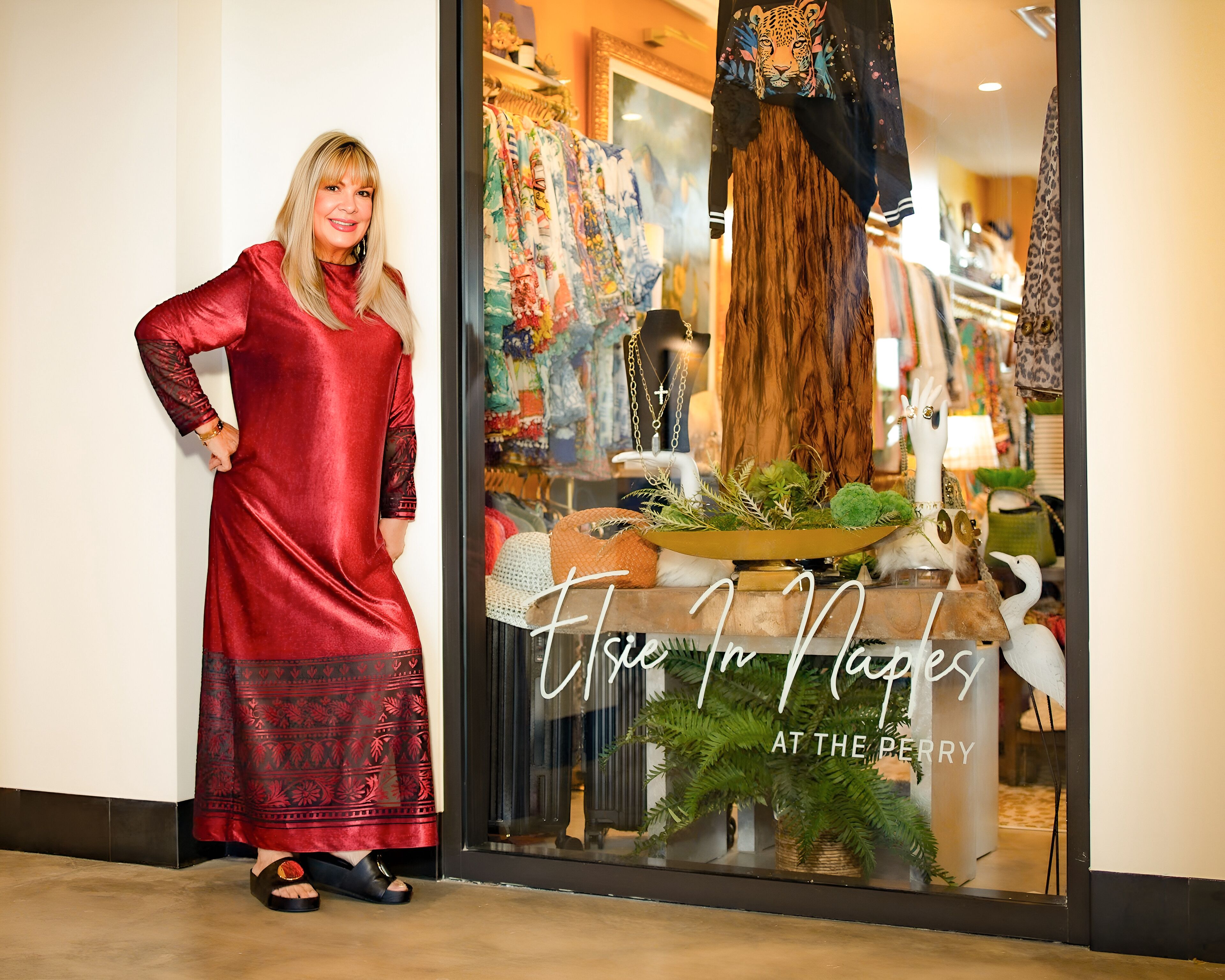 Une femme vêtue d’une robe rouge se tient devant la vitrine d’un magasin, sur laquelle on peut lire : « Vivez à Naples, au Berry ».