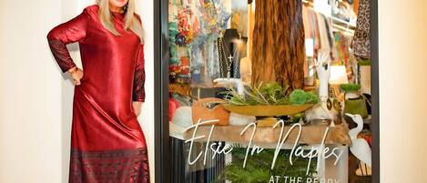 Une femme vêtue d’une robe rouge se tient devant la vitrine d’un magasin, sur laquelle on peut lire : « Vivez à Naples, au Berry ».