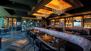 A restaurant with wooden tables, a floral bench, and hanging lights. - The Perry Hotel Naples (Naples)