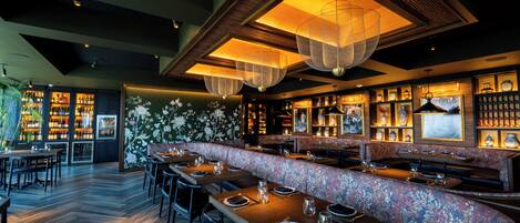 A restaurant with wooden tables, a floral bench, and hanging lights.