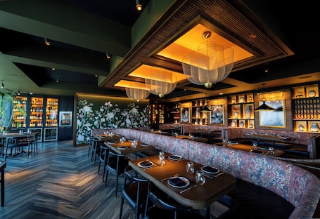 A restaurant with wooden tables, a floral bench, and hanging lights.