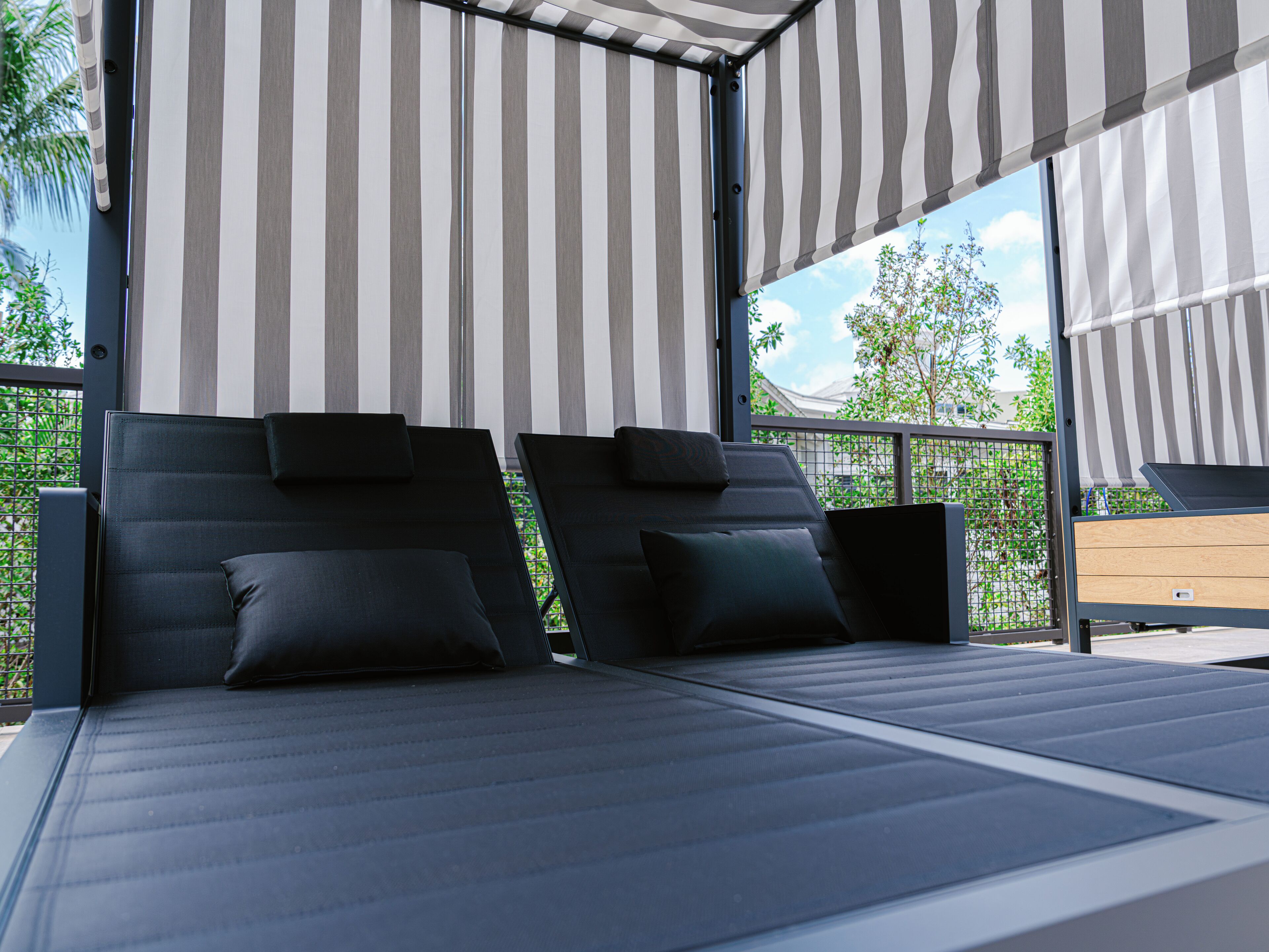 Une chambre à coucher moderne en plein air, avec deux lits noirs, des auvents à rayures et une vue sur la verdure.