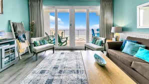 A spacious living room with a large sliding glass door leading to a balcony, a sofa set, a coffee table, and a TV stand. - Laketown Wharf 1326 (Panama City Beach)