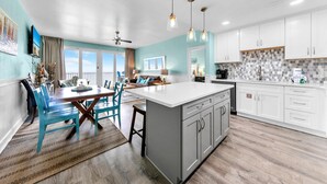 A modern kitchen with a central island, white cabinetry, and a dining area with blue chairs. - Laketown Wharf 1326 (Panama City Beach)