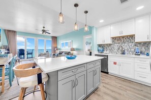 A modern kitchen with a large island, white cabinets, and a view to the outside.