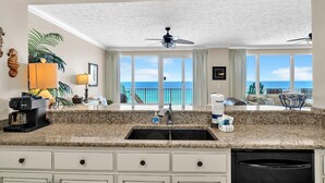 A kitchen with granite countertops, white cabinets, a black dishwasher, and a view of the ocean through large windows. - Hidden Dunes 602 (Panama City Beach)