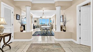 A spacious hallway with a dining area, featuring a chandelier, columns, and a view to the outside. - Hidden Dunes 602 (Panama City Beach)