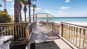 A wooden boardwalk leading to a beach with palm trees and a clear blue sky. - Hidden Dunes 403 (Panama City Beach)