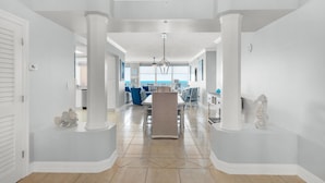 A spacious hallway with white walls and columns, leading to a dining area with a view of the ocean. - Hidden Dunes 403 (Panama City Beach)