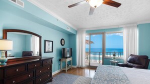 A bedroom with a large bed, a dresser, a TV, and a balcony with a view of the ocean. - Hidden Dunes 402 (Panama City Beach)